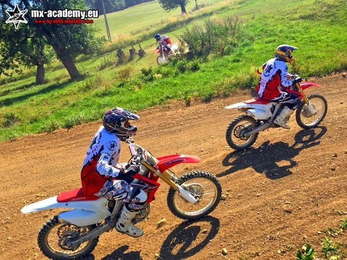 Try motocross: two riders out on the track, with a row of trees in the background