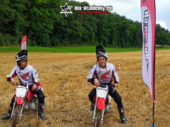 Women's motocross: two female riders sit on their bikes while flags fly in the background