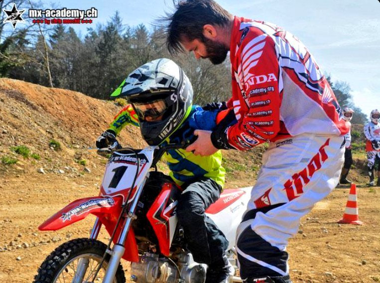 Motocross Schnupperkurs: Trainer hilft einem kleinen Kind mit der Startnummer 1 auf dem Bike